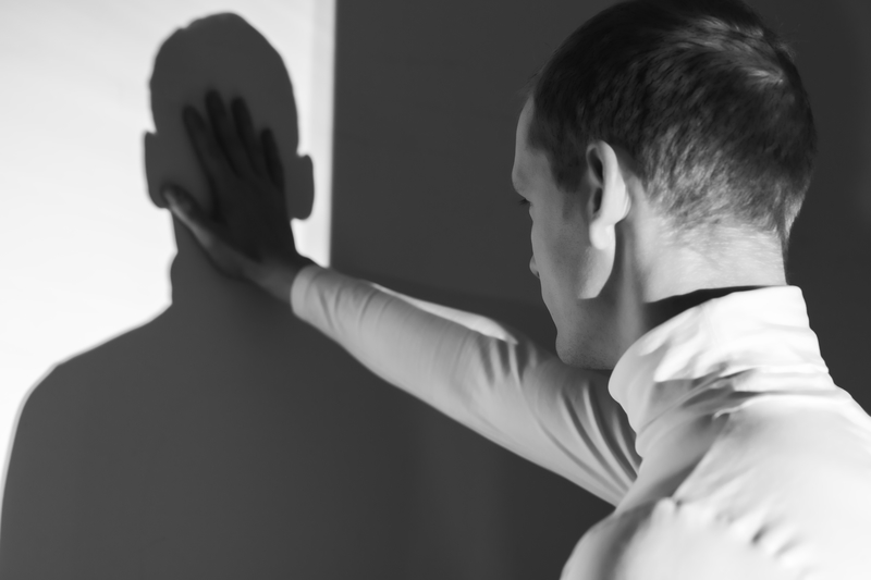 Black and white picture of a man putting his hand onto his own shadow in disgust.