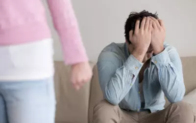 ending-relationship-break-up-therapy Man sitting on couch holding hands over his face as his partner walks away angrily.